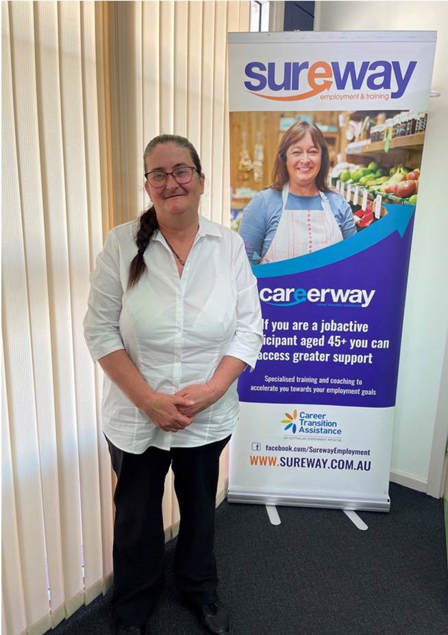 Christine stands in front of a Sureway banner inside the Sureway Port Pirie office wearing a crisp white short and black trousers