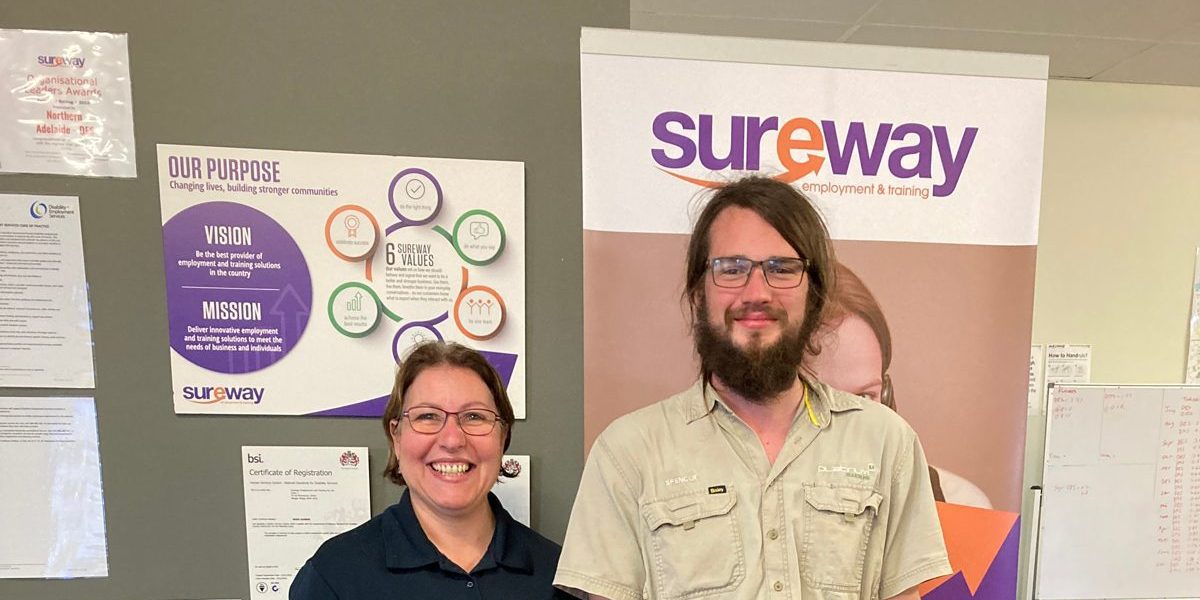 Spencer stands in front of a Sureway banner with his Consultant Lucia in the Sureway office