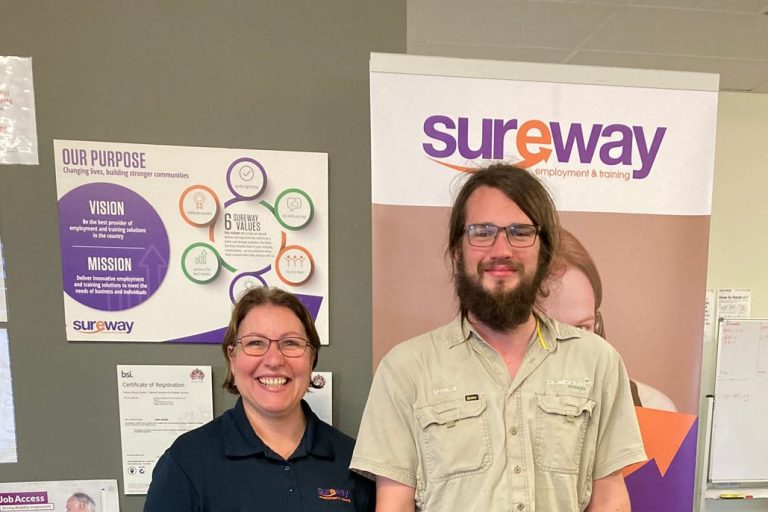 Spencer stands in front of a Sureway banner with his Consultant Lucia in the Sureway office